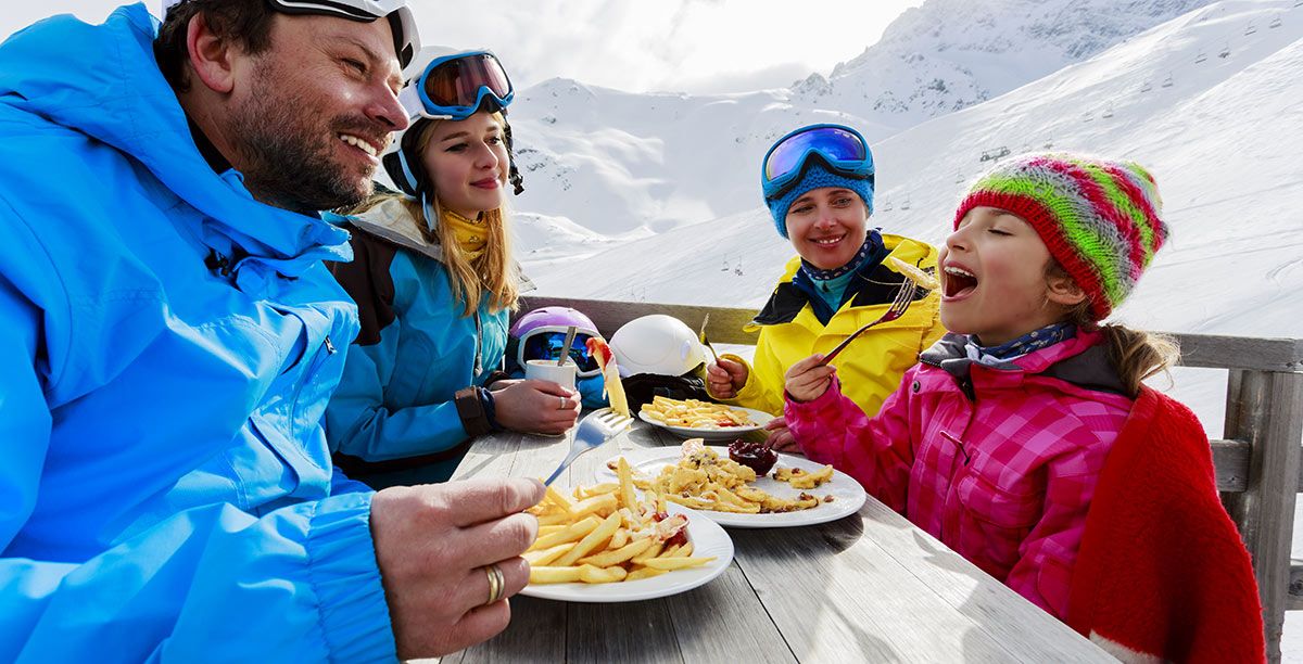 Mom, dad and two daughters eat something after skiing on the snow